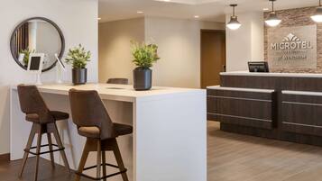 A reception area with a modern design, featuring a reception desk, two bar stools, a large mirror, and potted plants.