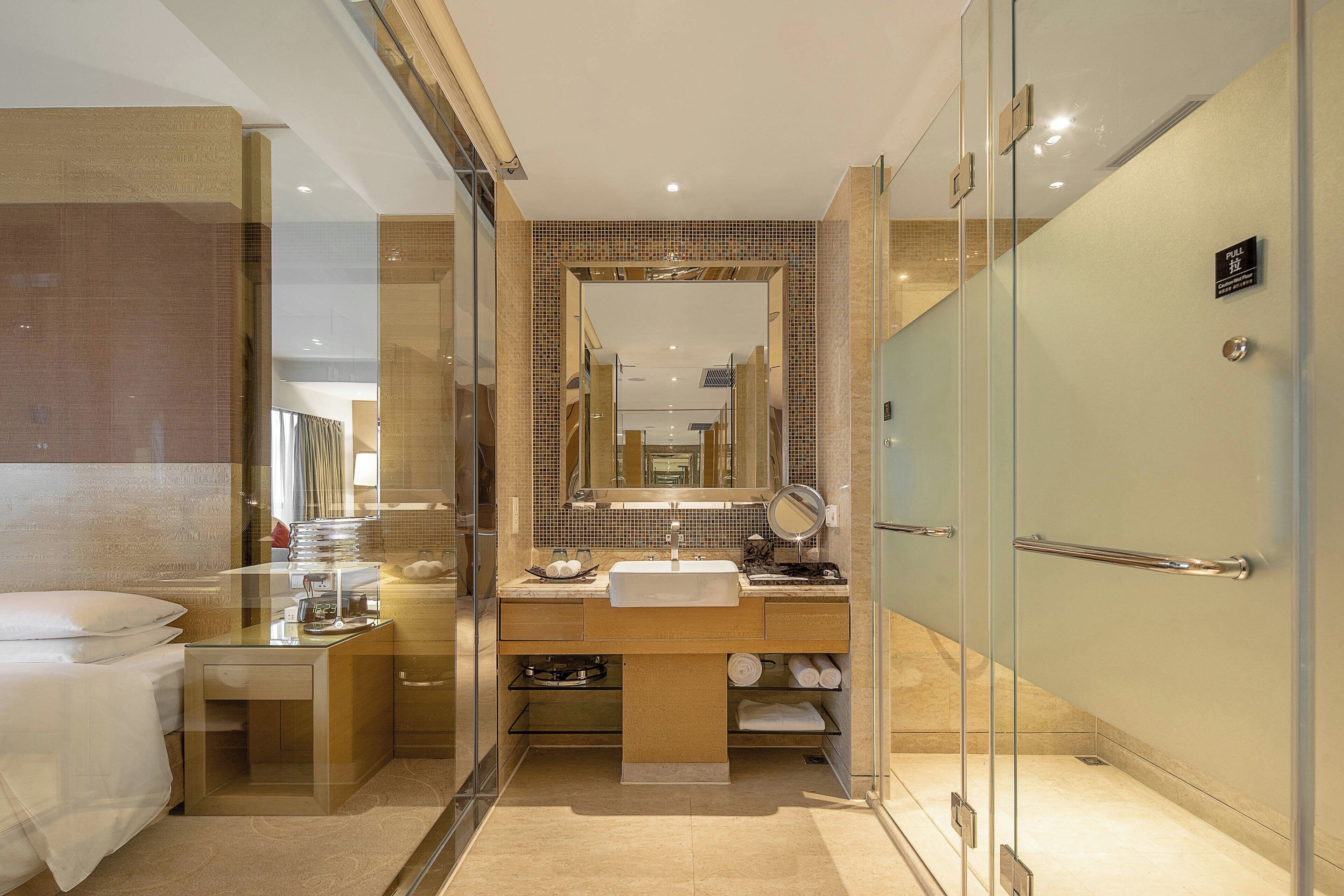 A modern bathroom with a glass shower enclosure, a large mirror, and a vanity with a sink and towel rack.