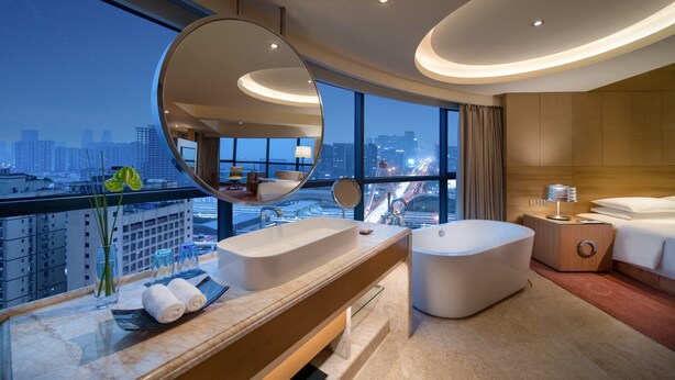 Een moderne hotelbadkamer met een ruime badkuip, een ronde spiegel en een wastafel met een groot wasbak.