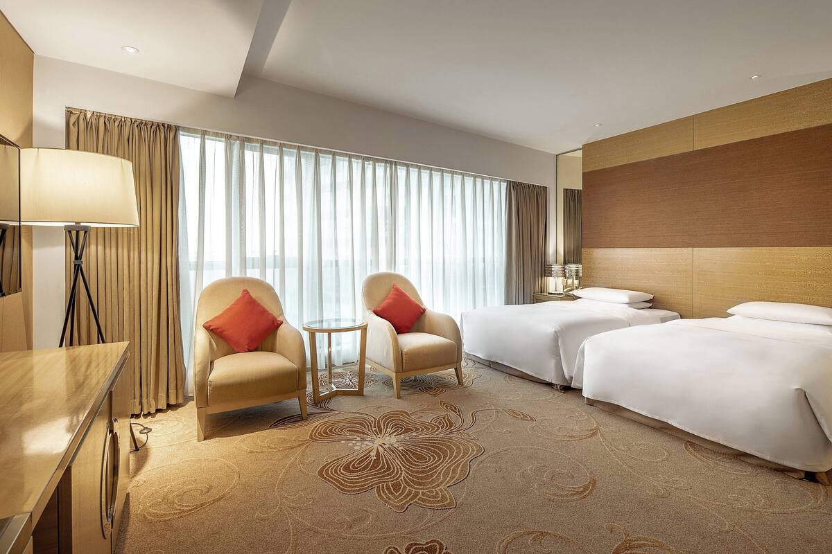 A hotel room with two single beds, a sofa, a small table, and a lamp.