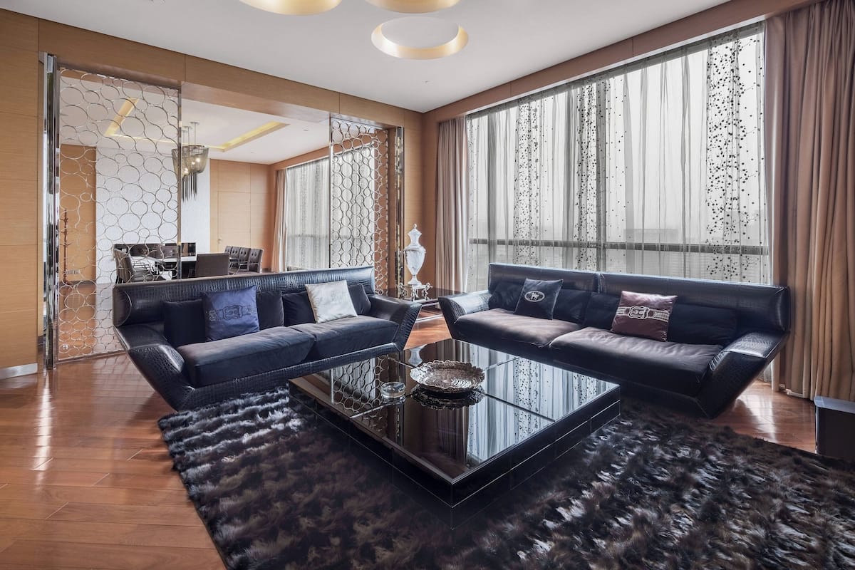 A modern living room with two dark sofas, a glass coffee table, and a fur rug.
