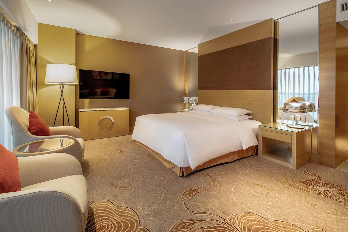 A hotel room with a large bed, a sofa, a bedside table, a lamp, and a TV.
