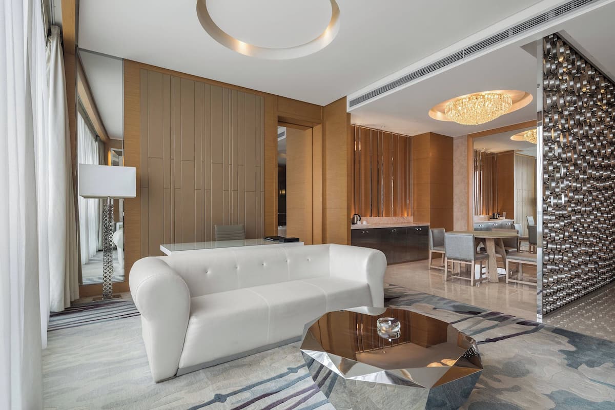 A modern hotel lobby with a white sofa, a round coffee table, and a dining area with a chandelier.
