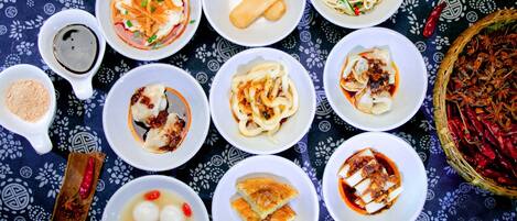 A table with various dishes, including dumplings, noodles, and a bowl of soup, set on a patterned tablecloth.