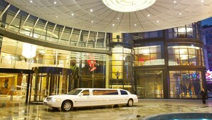 Een modern hotelinterieur met een rond plafondontwerp, een zwembad in het midden en een witte limousine geparkeerd buiten.