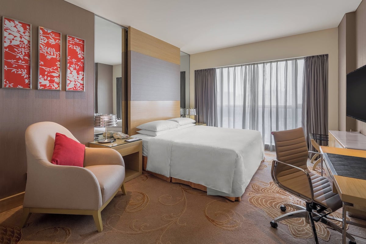 A hotel room with a bed, a desk, a chair, a TV, and a window with curtains.