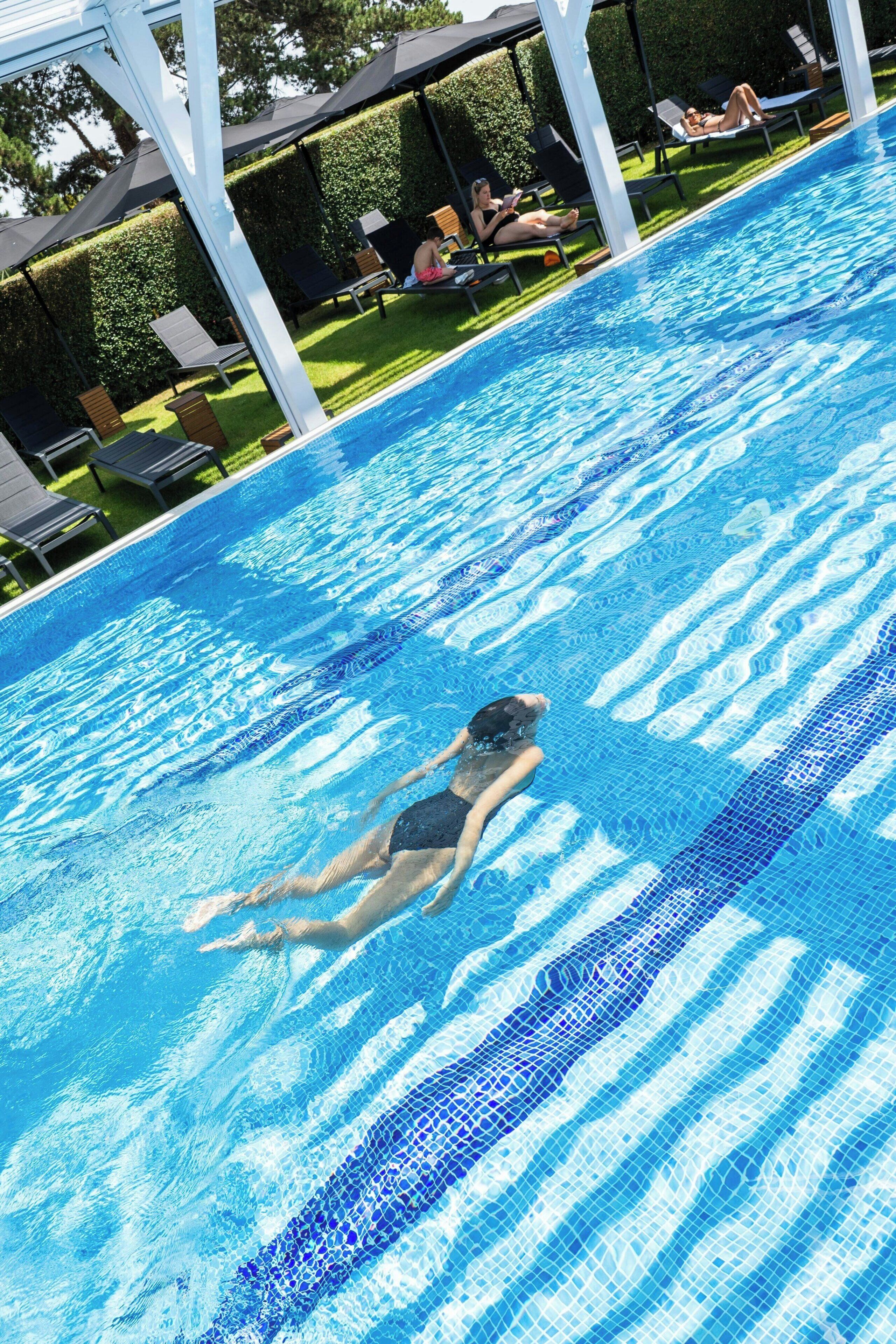 Une piscine où une personne nage, des chaises longues et un espace abrité.