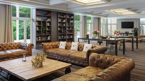 A spacious living room with leather sofas, a wooden coffee table, and a large bookshelf. - Renaissance Paris Hippodrome De St. Cloud Hotel (Rueil-Malmaison)