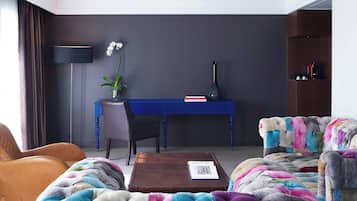 Un salon moderne avec un bureau bleu, un fauteuil en cuir marron, un canapé coloré et une table basse.