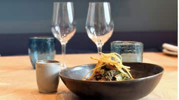 A dining table with a bowl of food, two wine glasses, and a small cup.