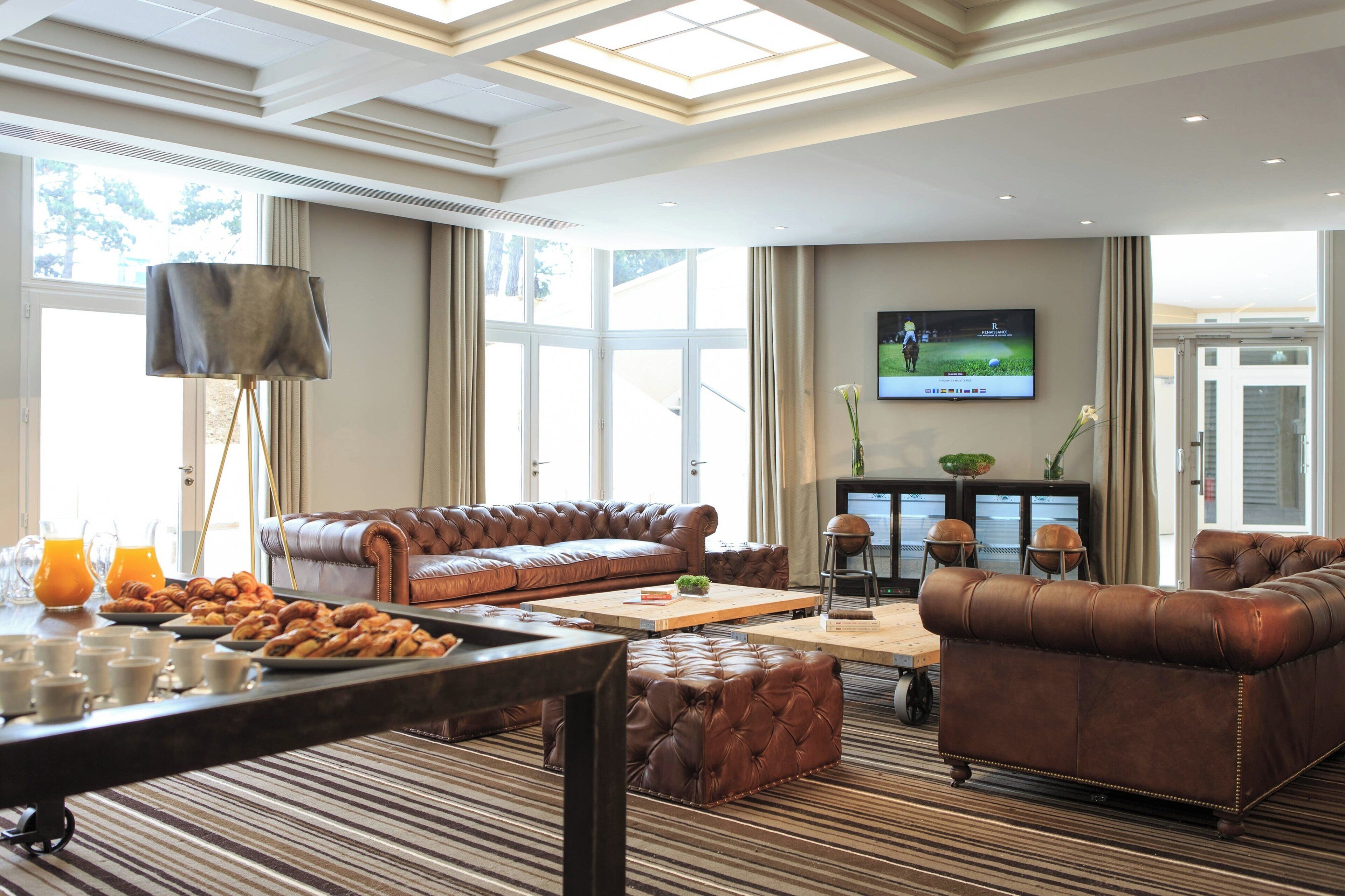 A spacious living room with a brown leather sofa, a coffee table, and a television mounted on the wall.