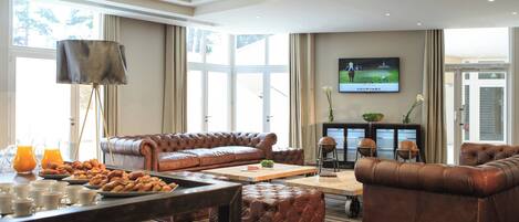 A spacious living room with a brown leather sofa, a coffee table, and a television mounted on the wall.
