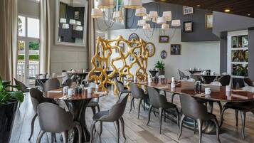 A modern dining area with round tables, grey chairs, and a decorative golden wall.