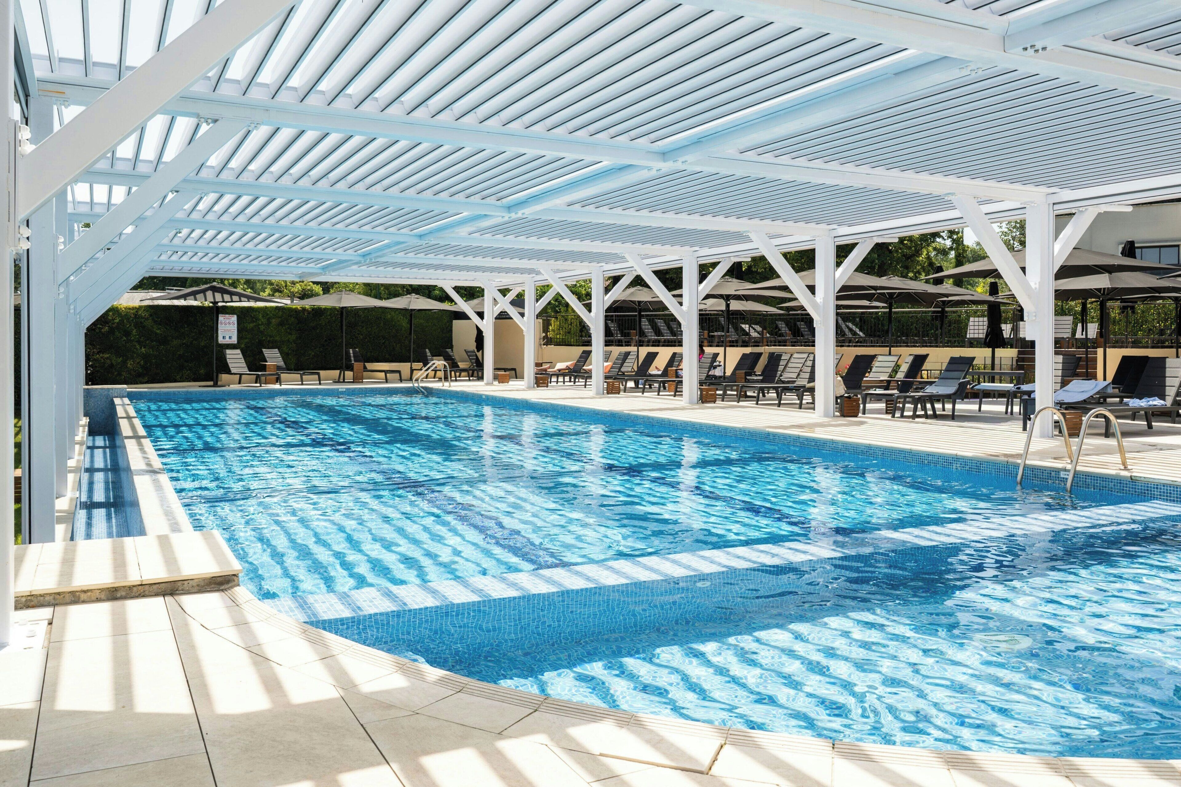 Una piscina con una pérgola blanca, tumbonas y una zona de terraza con baldosas.