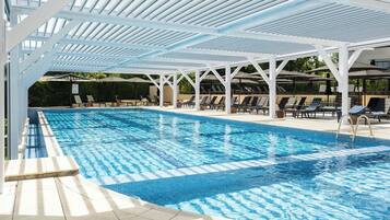 Una piscina con una pérgola blanca, tumbonas y una zona de terraza con baldosas.