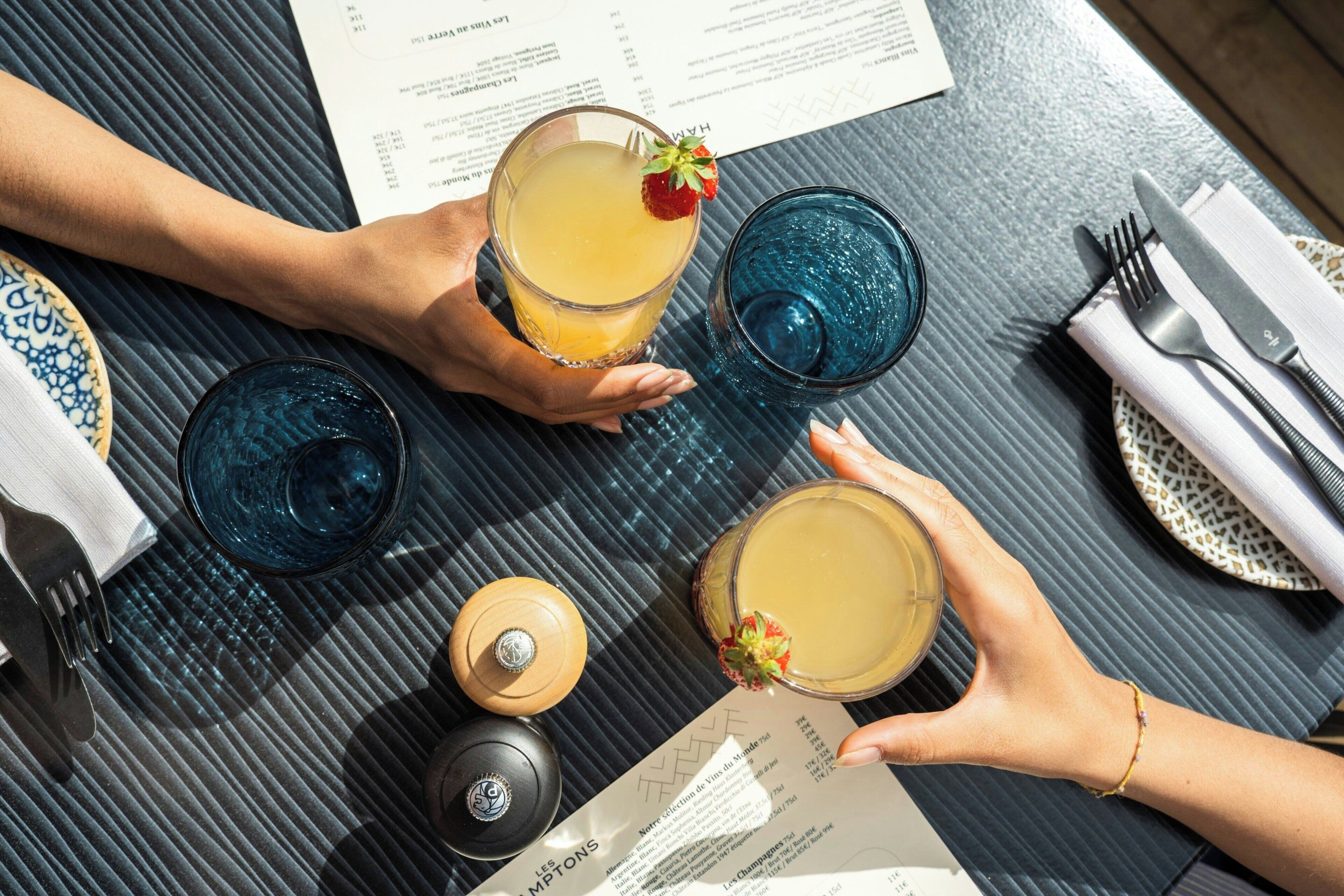 Une table avec un menu, trois verres contenant une boisson jaune et une bouteille d’eau.