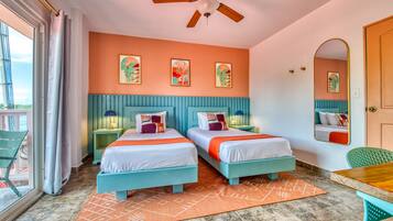 A bedroom with two beds, a ceiling fan, a large window, and artwork on the walls.
