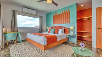 Une chambre d’hôtel avec un lit, un bureau, une chaise, une petite table avec un vase et un ventilateur de plafond.