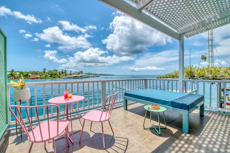 A balcony with a view of the sea, a table with chairs, and a bench.