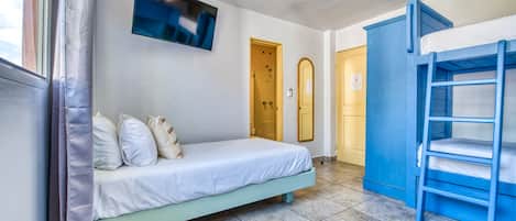 A room with a bed, a bunk bed, a ceiling fan, a TV, and a door.