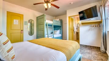 Habitación de hotel con cama, ventilador de techo, televisor y armario.