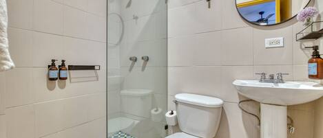 A bathroom with a toilet, sink, shower, and a glass-enclosed shower stall.