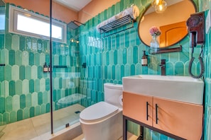 Un baño con cabina de ducha de vidrio, inodoro blanco y lavabo con espejo.