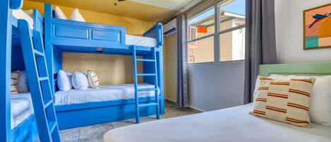 A room with bunk beds, a ceiling fan, and a large window with curtains.