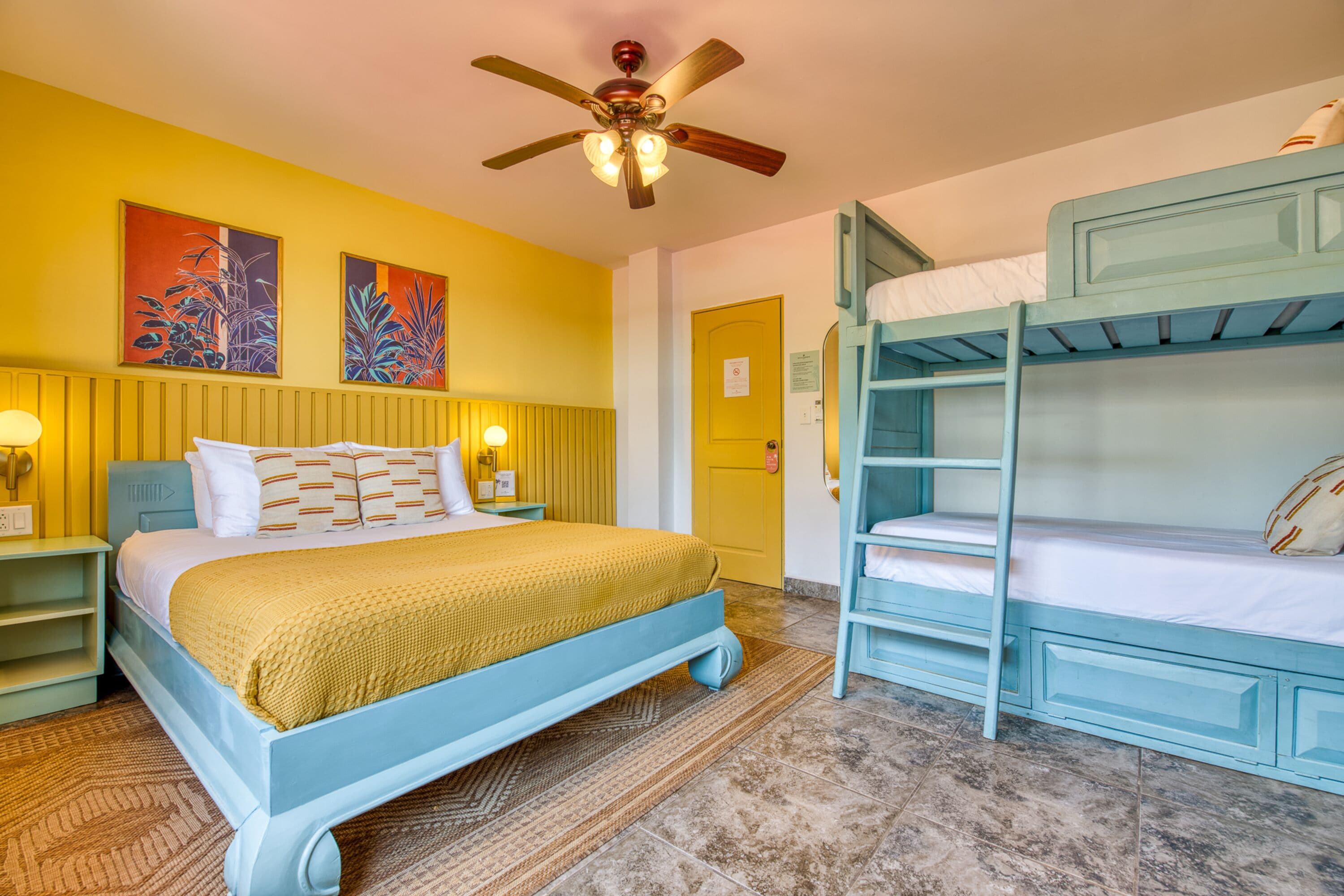 A room with a bed, bunk beds, a ceiling fan, and artwork on the wall.