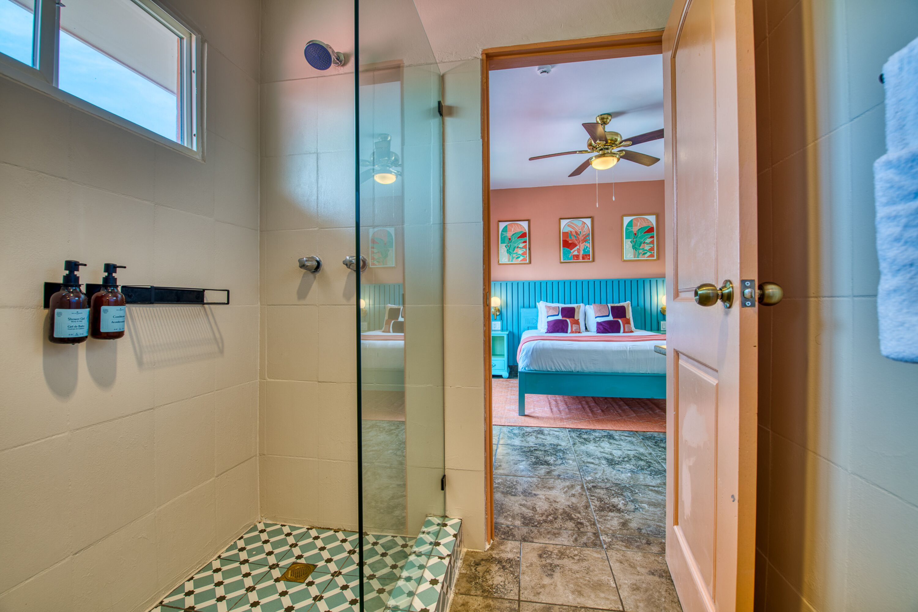 Une chambre d’hôtel dotée d’une douche en verre, d’un lit avec une literie de couleur turquoise et d’un ventilateur de plafond.