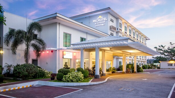 A modern hotel with a covered entrance, palm trees, and bicycles parked outside.