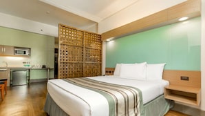 A hotel room with a bed, a wooden headboard, a kitchenette, and a partition wall.