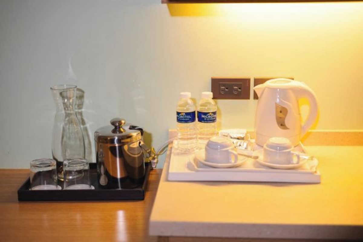 A hotel room's breakfast setup with a coffee maker, tea pot, water bottles, and a tray with cups and saucers.