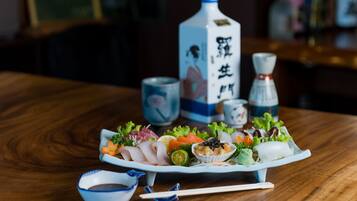 Una mesa de madera con un plato de sashimi, una botella de sake y un recipiente pequeño de salsa de soja.