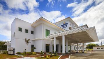 A modern microhotel with a covered entrance, white exterior, and a landscaped garden area.