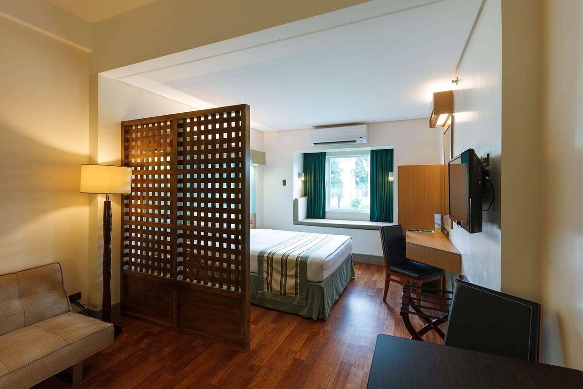 A hotel room with a bed, desk, chair, and a wooden partition.