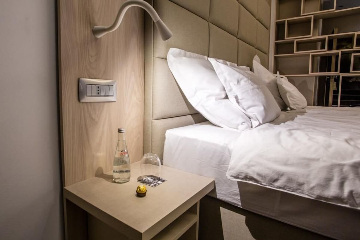 A hotel room with a bed, bedside table, lamp, and built-in shelving.