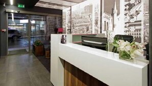 A reception area with a glass door entrance, a reception desk, and a wall with printed images. - Colors Inn (Sarajevo)