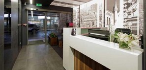 A reception area with a glass door entrance, a reception desk, and a wall with printed images. - Colors Inn (Sarajevo)