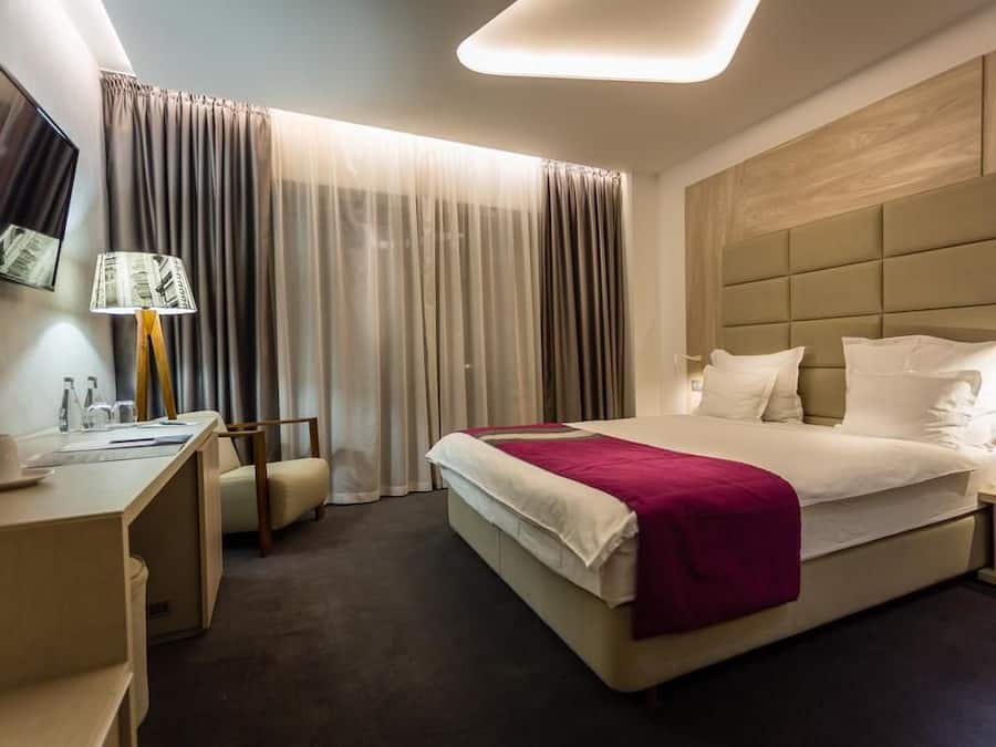 A hotel room with a bed, bedside table, lamp, chair, and curtains.