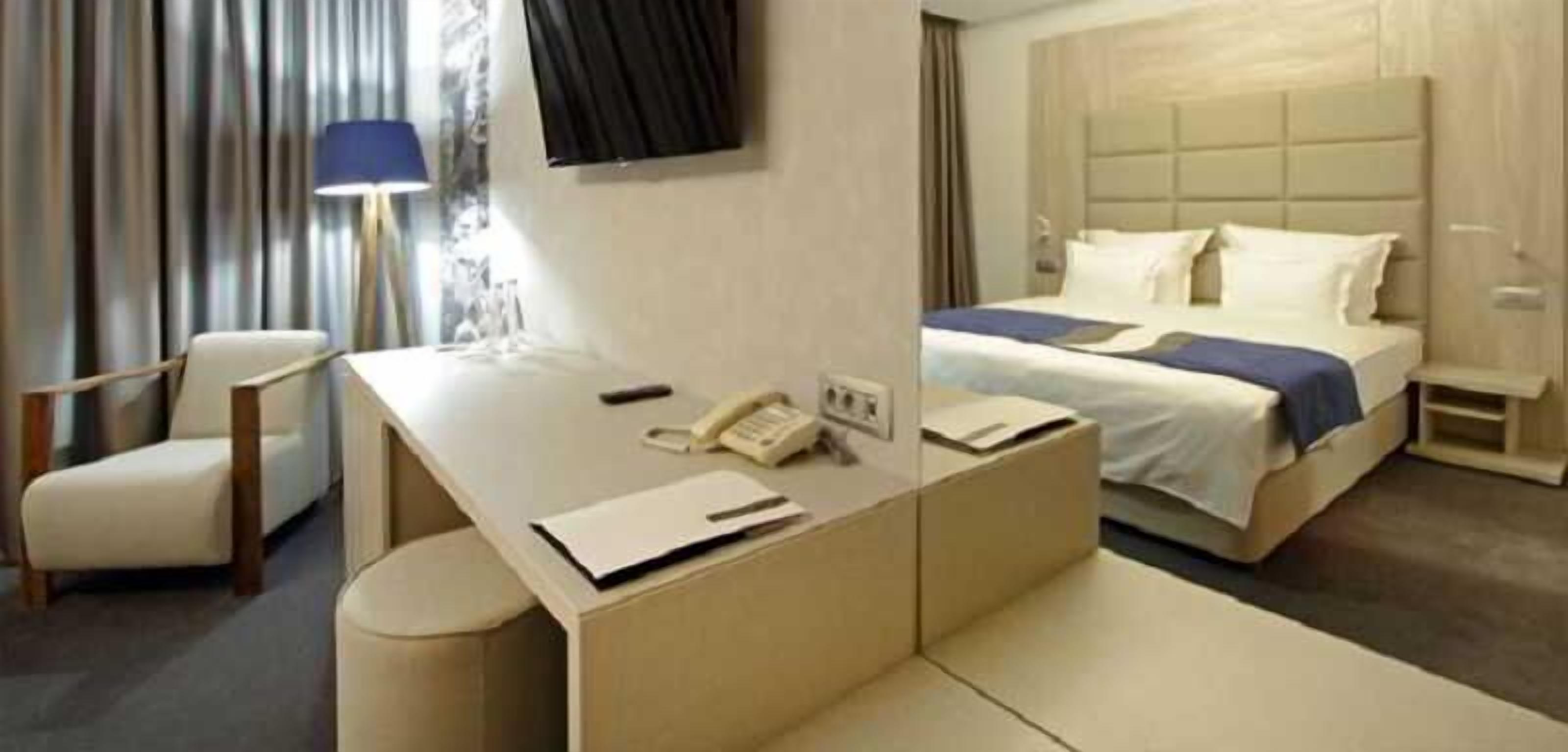 A hotel room with a bed, a desk with a telephone, a chair, and a lamp.
