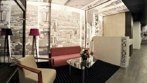 A modern hotel room with a cityscape view, a red sofa, a glass table, and a lamp. - Colors Inn (Sarajevo)