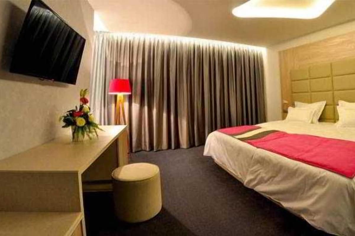 A hotel room with a bed, a desk, a chair, a TV, and curtains.