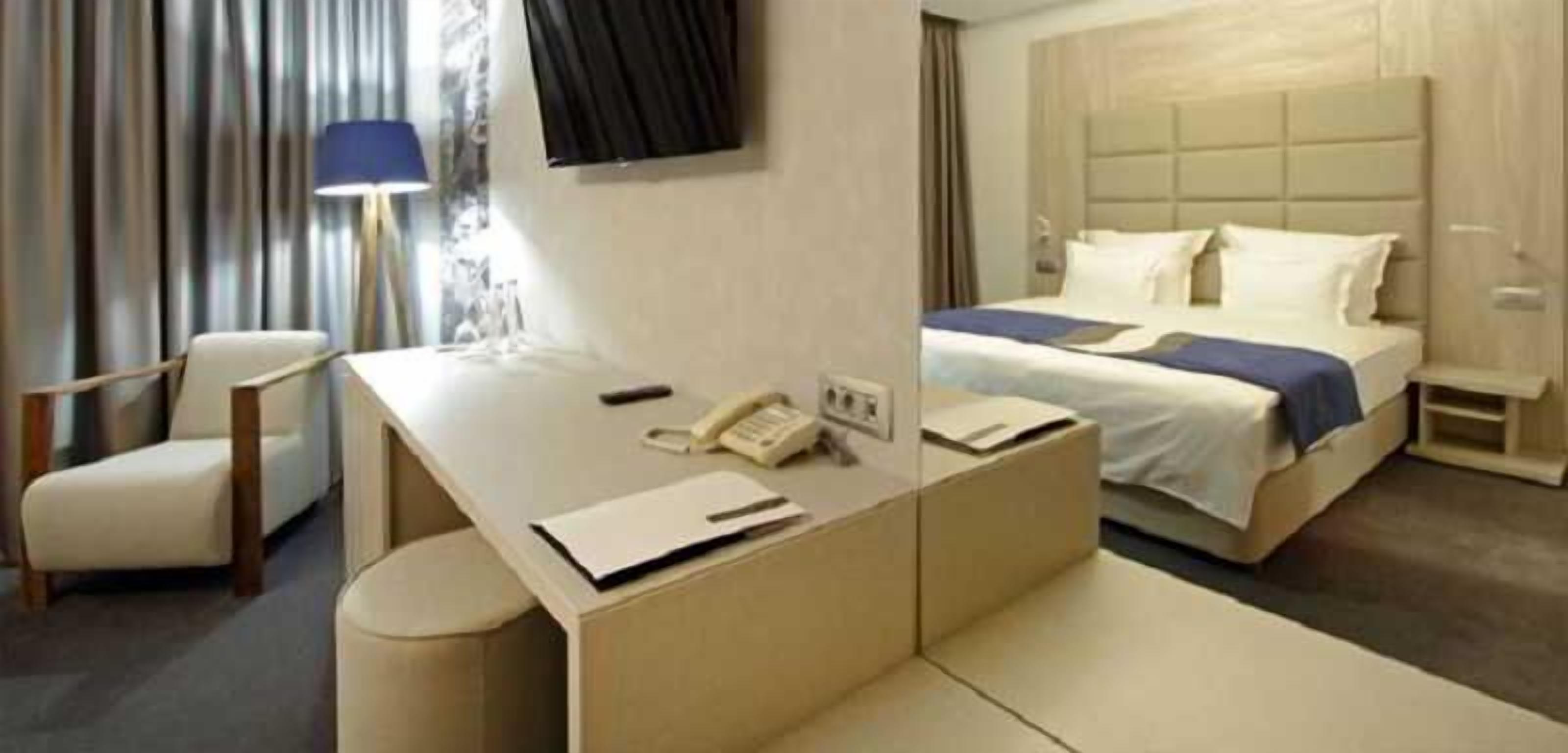 A hotel room with a bed, a desk with a telephone, a chair, and a lamp.