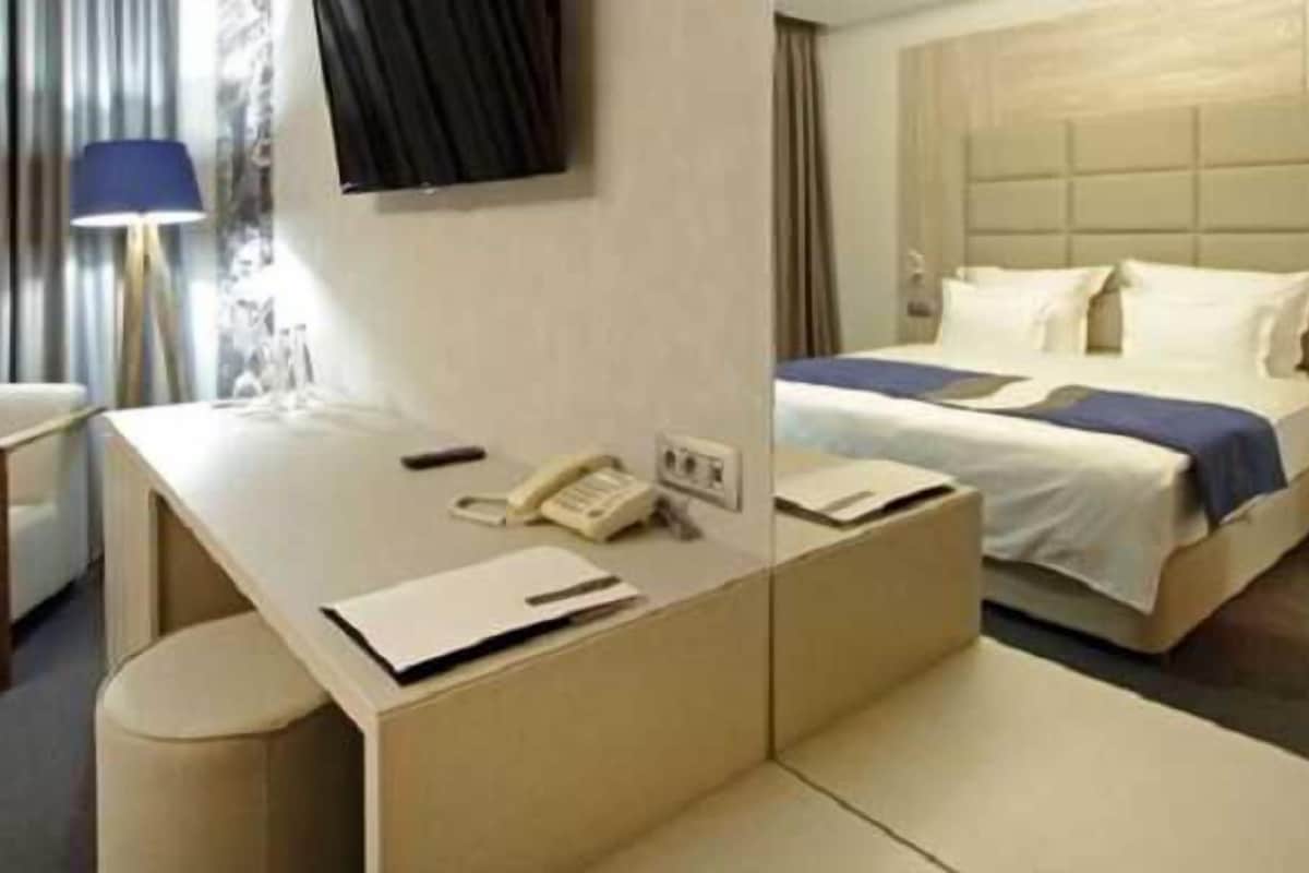 A hotel room with a bed, a desk with a telephone, a chair, and a lamp.