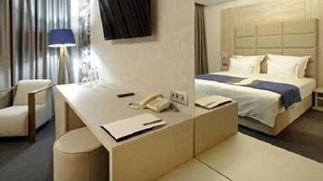 A hotel room with a bed, a desk with a telephone, a chair, and a lamp.
