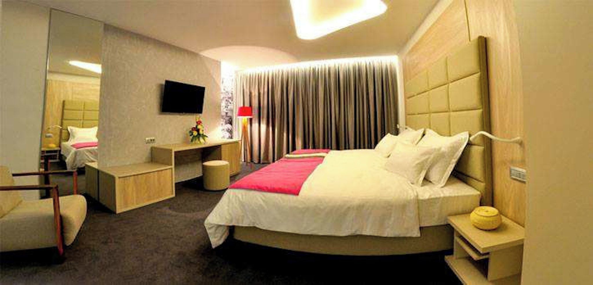 Una habitación de hotel moderna con una cama curvada, mesitas de noche, un televisor de pantalla plana y un espejo grande.