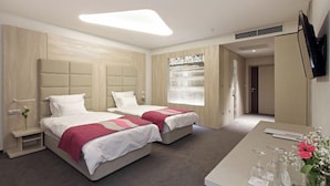 A hotel room with two beds, a desk, a TV, and a window with a view.