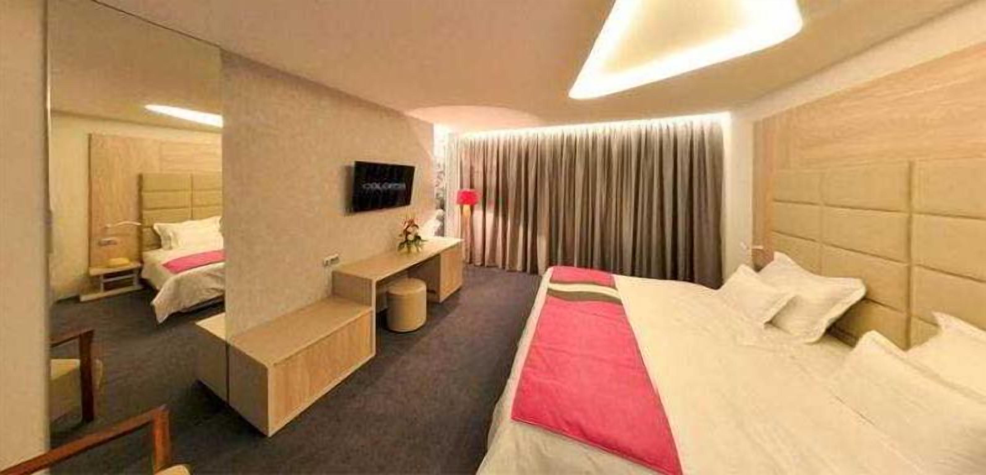 Une chambre d’hôtel moderne équipée d’un grand lit, d’un bureau, d’une chaise, d’une télévision et d’un miroir.