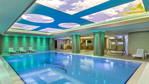 An indoor swimming pool with a ceiling mural, green ambient lighting, and lounge chairs. - Ramada by Wyndham Usak (Usak)